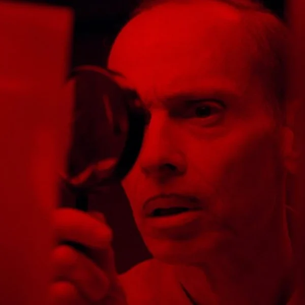 pete peters played by john waters inspecting an photo in seed of chucky 1