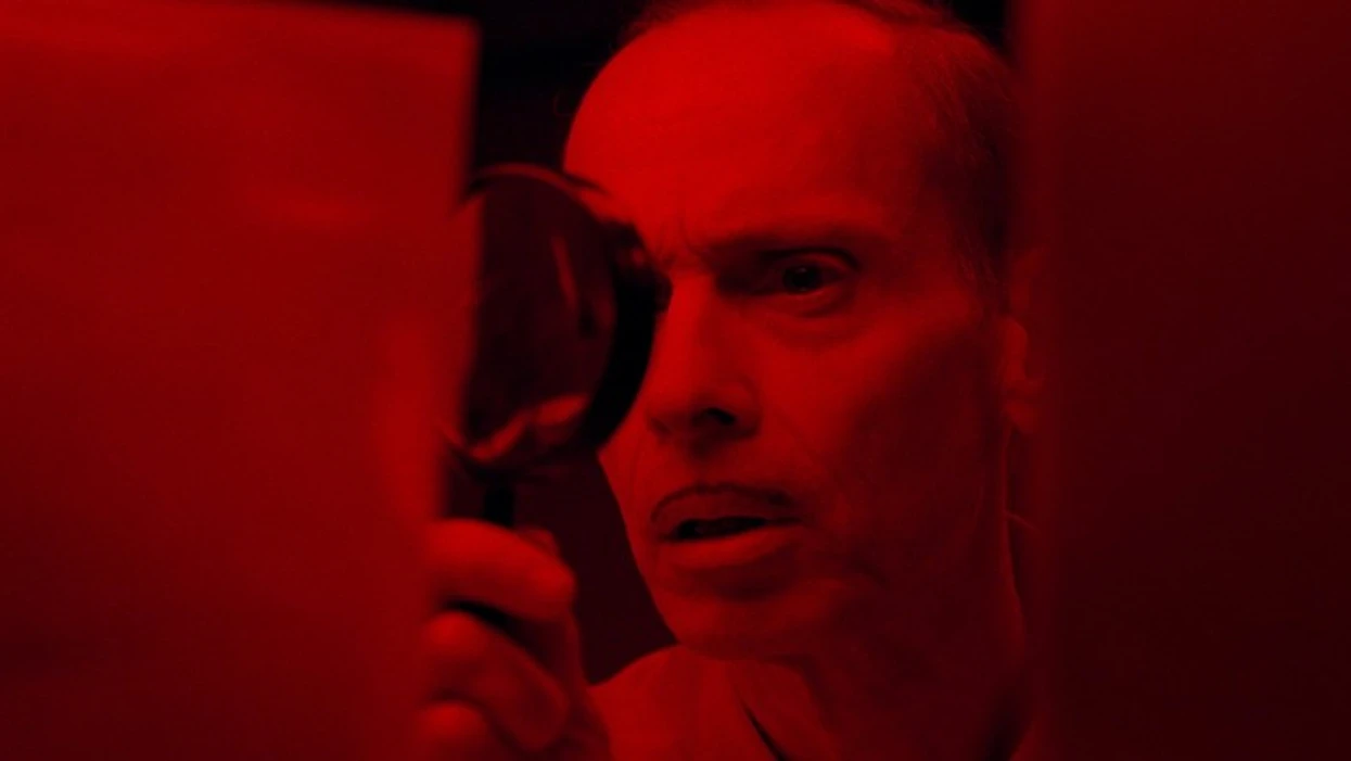 pete peters played by john waters inspecting an photo in seed of chucky 1